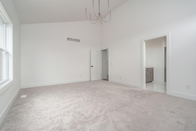 carpeted spare room with an inviting chandelier and high vaulted ceiling