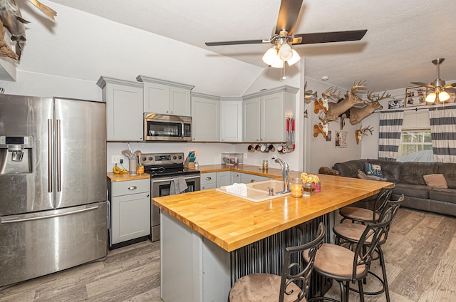 kitchen with appliances with stainless steel finishes, light hardwood / wood-style floors, a breakfast bar, butcher block countertops, and ceiling fan