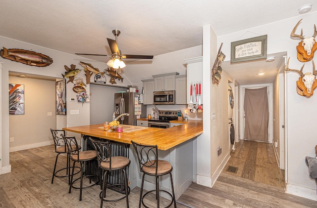 kitchen with wooden counters, a kitchen breakfast bar, stainless steel appliances, light wood-type flooring, and stacked washer / drying machine