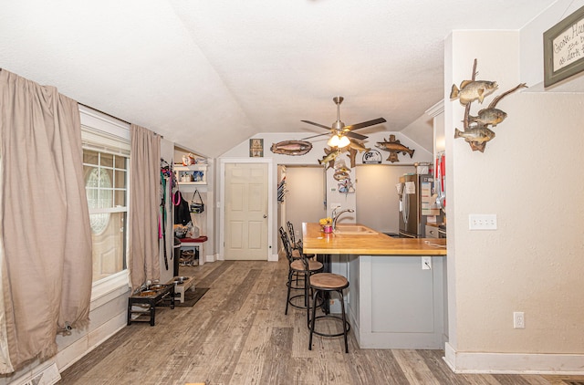 kitchen with stainless steel fridge, a kitchen bar, vaulted ceiling, and butcher block counters