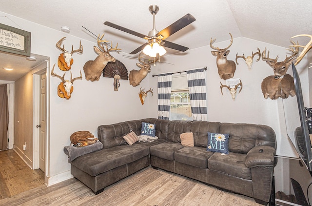 living room featuring light hardwood / wood-style flooring, vaulted ceiling, ceiling fan, and a textured ceiling