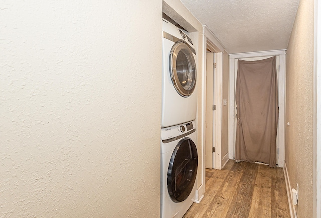 laundry area with light hardwood / wood-style flooring, a textured ceiling, and stacked washer and clothes dryer