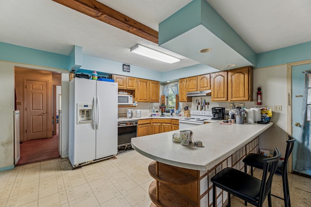 kitchen featuring a breakfast bar, white appliances, kitchen peninsula, and a textured ceiling