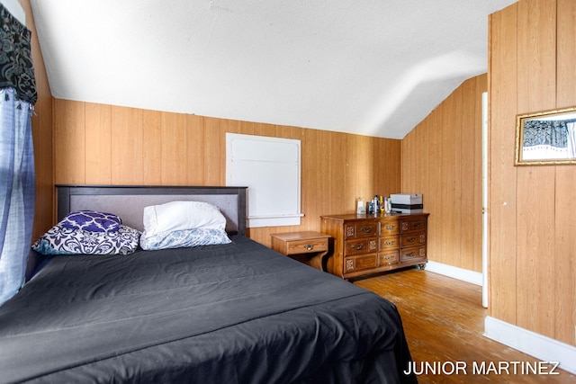 bedroom featuring wooden walls, light hardwood / wood-style floors, and vaulted ceiling