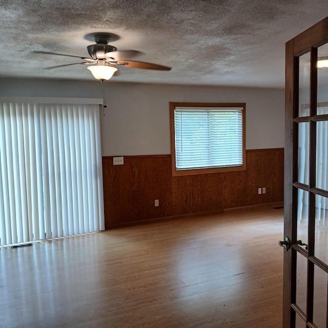 unfurnished room featuring a textured ceiling, wooden walls, ceiling fan, and light hardwood / wood-style flooring