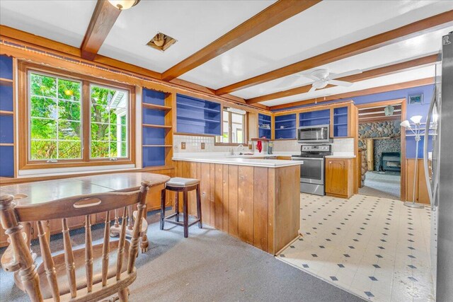 kitchen featuring beamed ceiling, a breakfast bar area, kitchen peninsula, stainless steel appliances, and ceiling fan