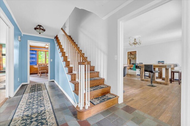 stairway with wood-type flooring, crown molding, and an inviting chandelier