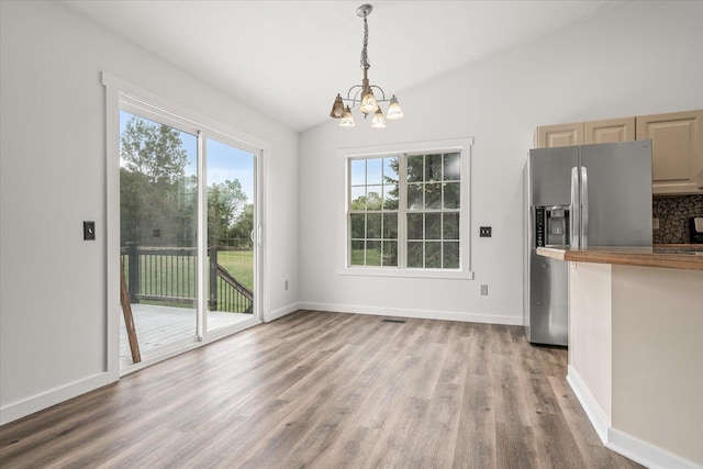 unfurnished dining area featuring hardwood / wood-style flooring, a chandelier, and vaulted ceiling