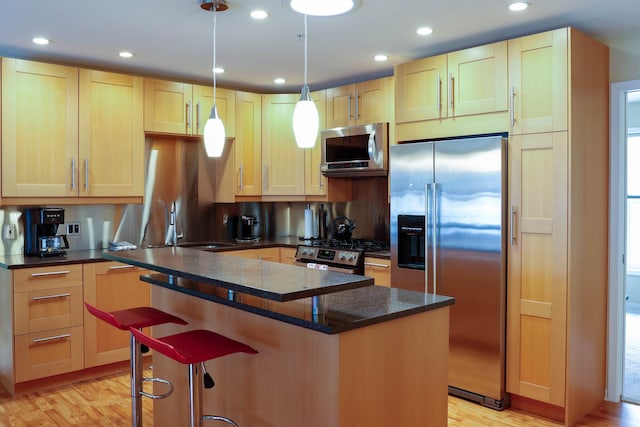 kitchen featuring appliances with stainless steel finishes, a kitchen island, light wood-type flooring, decorative light fixtures, and dark stone counters