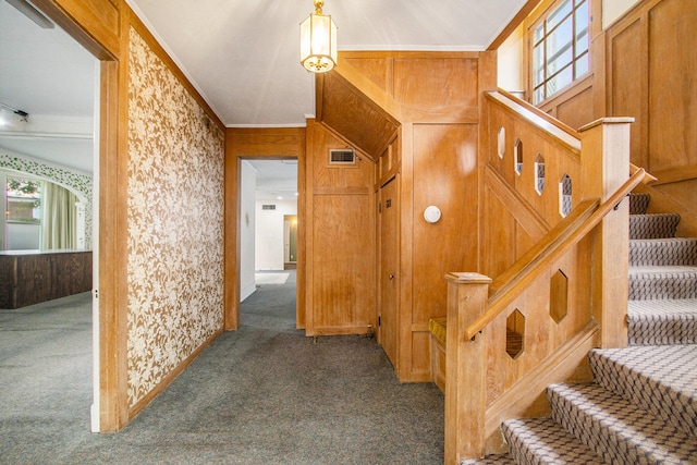 hallway with wood walls, ornamental molding, and dark colored carpet