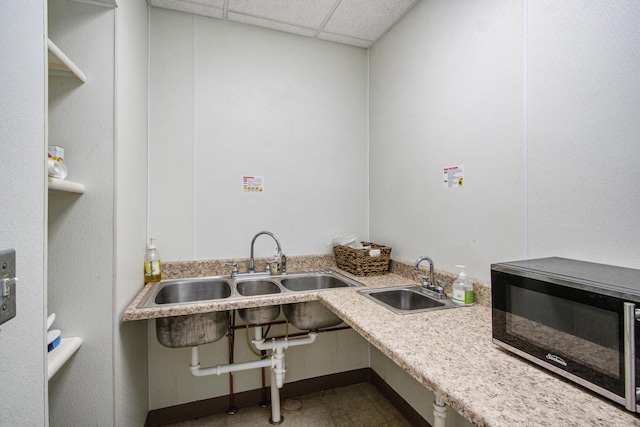 kitchen with a drop ceiling, light stone counters, and sink