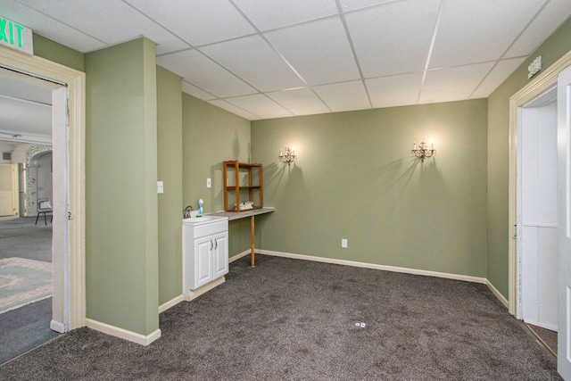 interior space featuring dark carpet, white cabinetry, a drop ceiling, and sink