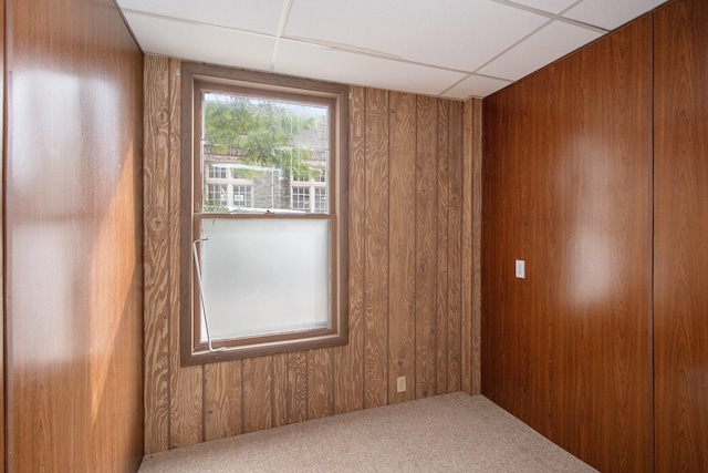 carpeted spare room featuring wood walls and a paneled ceiling