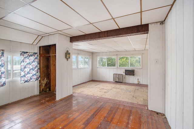 interior space with wood-type flooring, a drop ceiling, wooden walls, and an AC wall unit