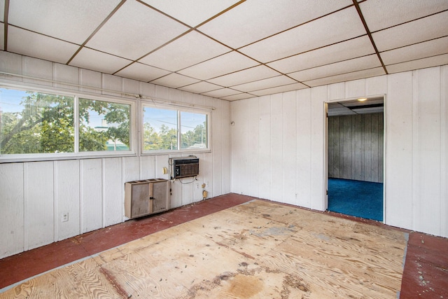 unfurnished living room featuring wooden walls, a paneled ceiling, and a wall unit AC