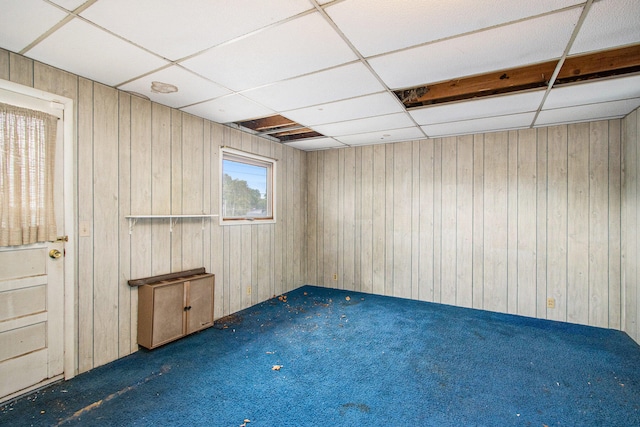 carpeted empty room with a drop ceiling and wooden walls