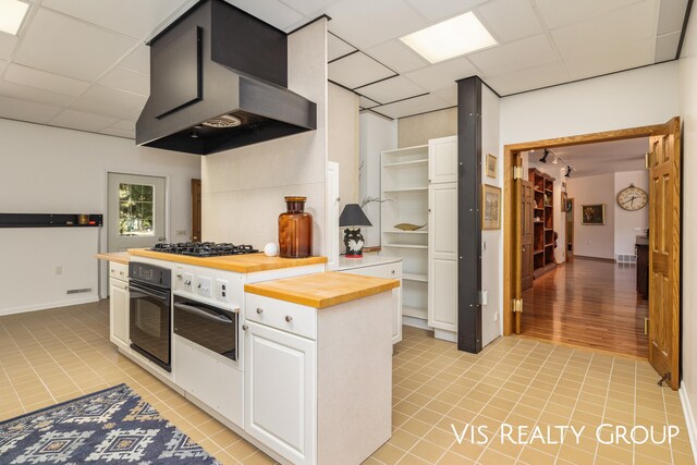 kitchen with white cabinets, wooden counters, exhaust hood, stainless steel appliances, and light hardwood / wood-style floors