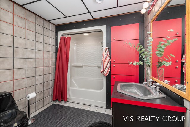 bathroom with tile walls, a drop ceiling, tile patterned floors, shower / bath combo with shower curtain, and vanity