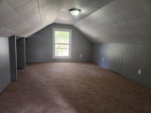 bonus room with carpet floors, lofted ceiling, and wooden walls