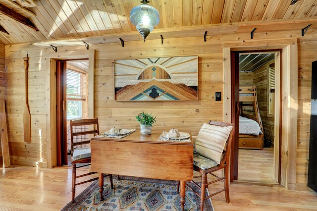 dining space with light wood-type flooring, wood ceiling, and wood walls