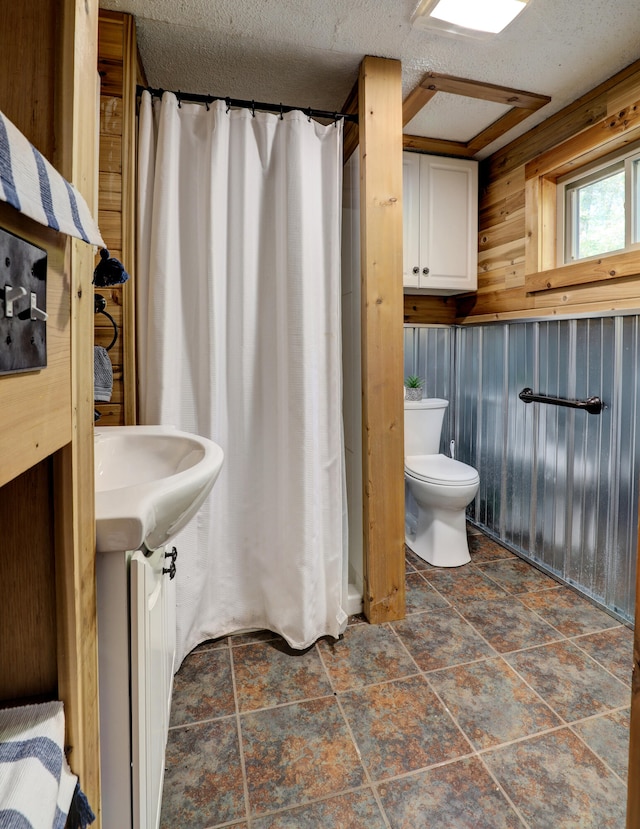 bathroom featuring a textured ceiling, wooden walls, and toilet