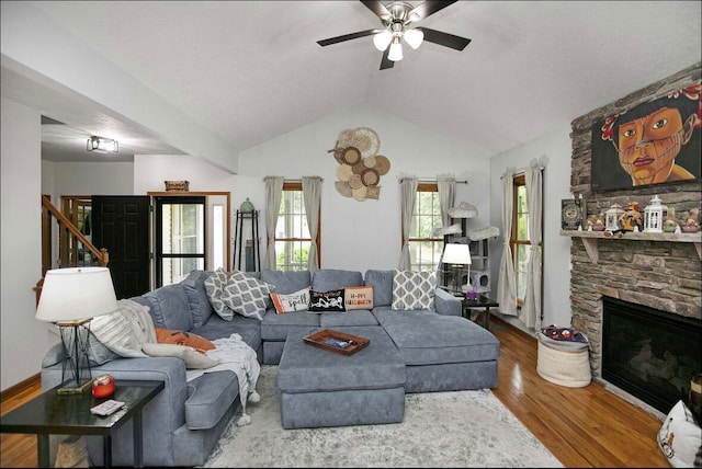 living room featuring wood-type flooring, a stone fireplace, lofted ceiling, and ceiling fan