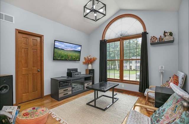 living room with a notable chandelier, vaulted ceiling, and light hardwood / wood-style floors