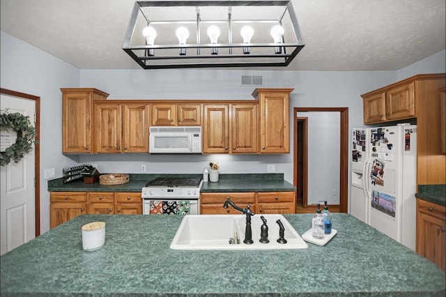 kitchen featuring white appliances, a textured ceiling, a kitchen island with sink, and sink