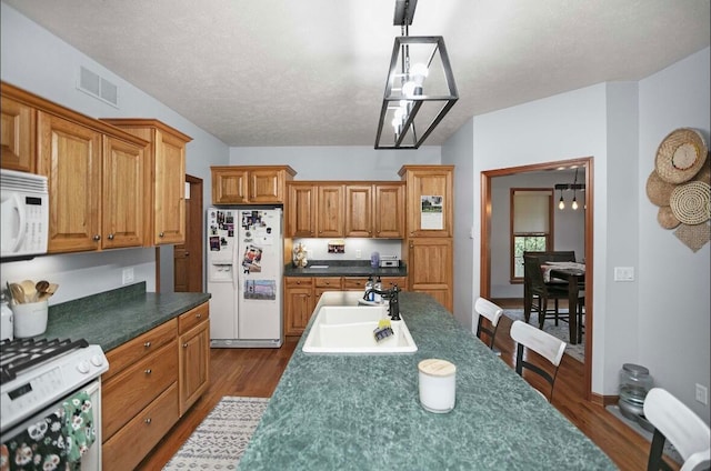 kitchen with sink, white appliances, a textured ceiling, decorative light fixtures, and dark hardwood / wood-style floors