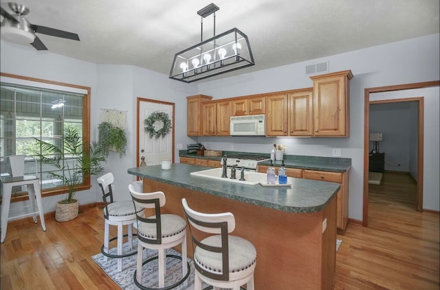 kitchen with a breakfast bar, pendant lighting, a kitchen island with sink, ceiling fan with notable chandelier, and light hardwood / wood-style flooring