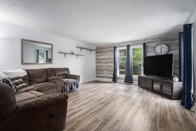 living room with a textured ceiling, wooden walls, and light hardwood / wood-style flooring