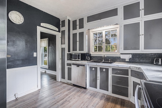 kitchen with appliances with stainless steel finishes, light wood-type flooring, sink, and decorative backsplash