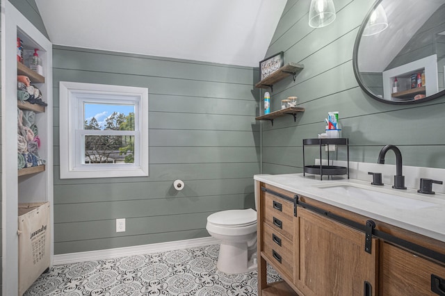 bathroom featuring wooden walls, vanity, lofted ceiling, and toilet