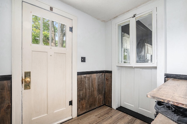 entryway with light wood-type flooring, a textured ceiling, and wooden walls