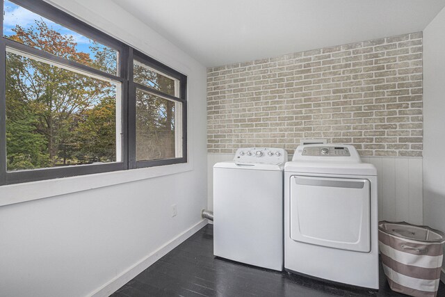 laundry room with brick wall, dark hardwood / wood-style floors, washer and dryer, and a wealth of natural light