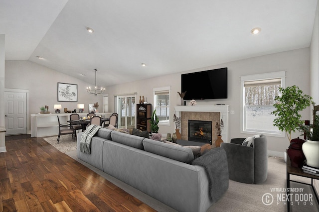 living room with a tiled fireplace, vaulted ceiling, dark wood-type flooring, and an inviting chandelier