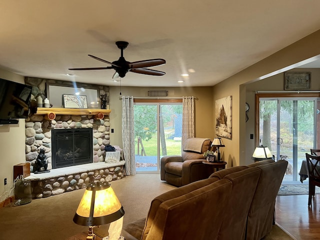 carpeted living room featuring a stone fireplace, ceiling fan, and a healthy amount of sunlight