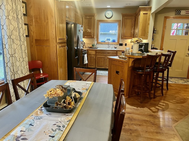 kitchen with a kitchen bar, stainless steel fridge, light wood-type flooring, tasteful backsplash, and sink