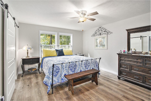 bedroom featuring ceiling fan, a barn door, a textured ceiling, and hardwood / wood-style flooring