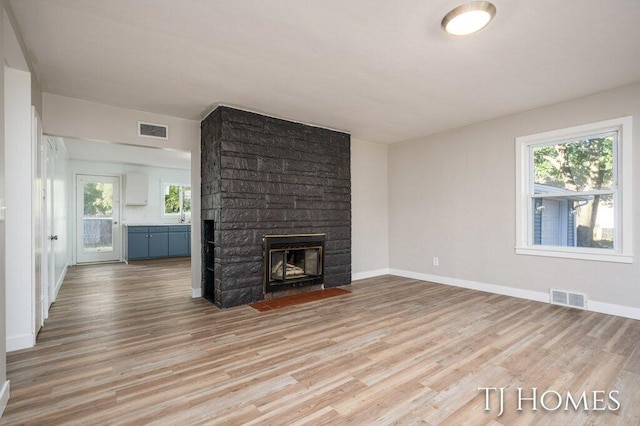 unfurnished living room with a stone fireplace, light wood-type flooring, and a healthy amount of sunlight