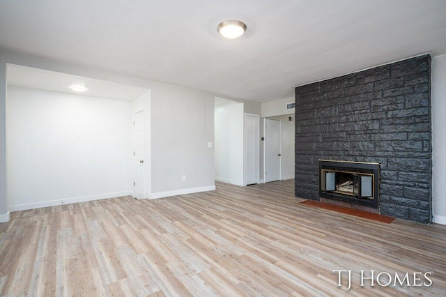 unfurnished living room with light wood-type flooring and a stone fireplace