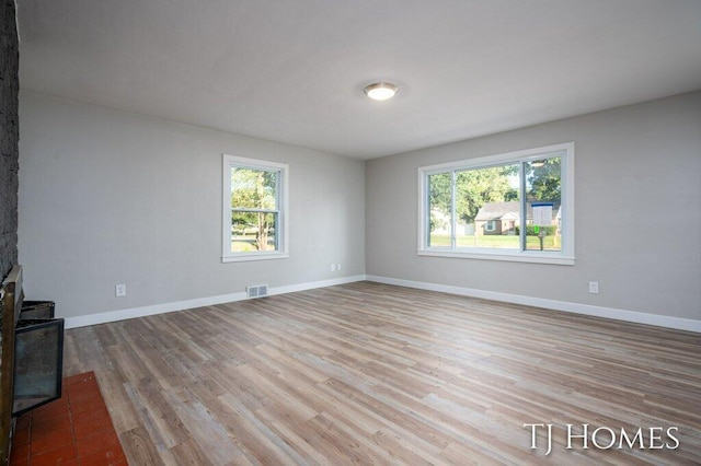 unfurnished living room featuring a stone fireplace, light hardwood / wood-style flooring, and plenty of natural light