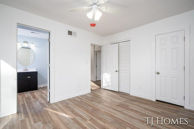 unfurnished bedroom featuring light wood-type flooring, sink, ceiling fan, and ensuite bathroom