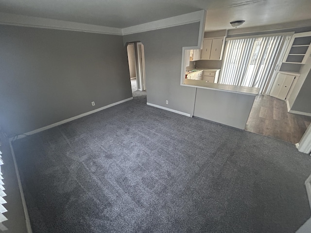 unfurnished living room featuring ornamental molding and dark colored carpet