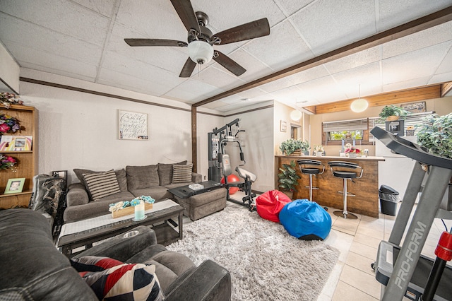 tiled living room with a paneled ceiling, ceiling fan, and bar area