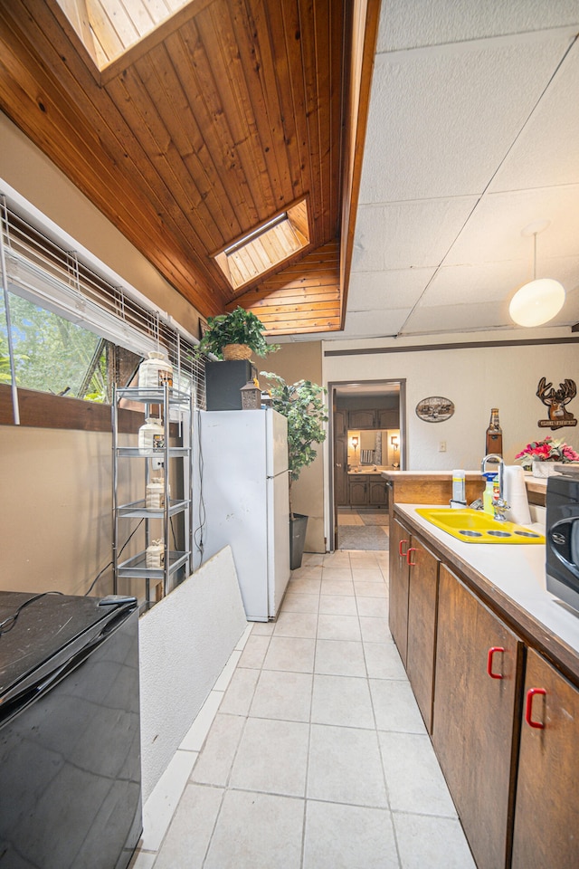 kitchen with sink, wood ceiling, vaulted ceiling with skylight, light tile patterned floors, and white refrigerator