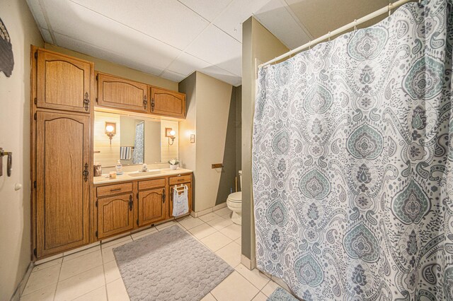 bathroom with vanity, toilet, tile patterned floors, and a drop ceiling