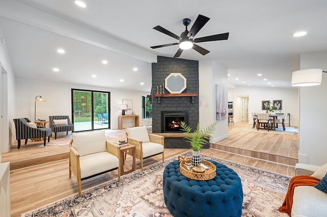 living room with light wood-type flooring, lofted ceiling, ceiling fan, and a fireplace