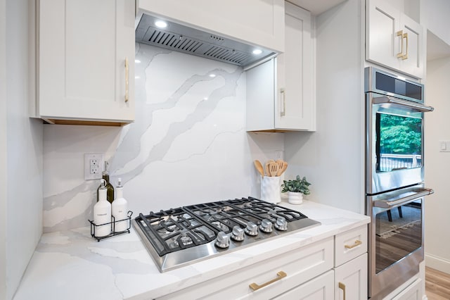 kitchen featuring light stone countertops, custom exhaust hood, appliances with stainless steel finishes, and white cabinetry