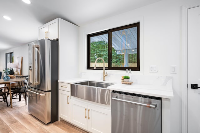 kitchen featuring sink, white cabinets, light hardwood / wood-style flooring, appliances with stainless steel finishes, and light stone countertops